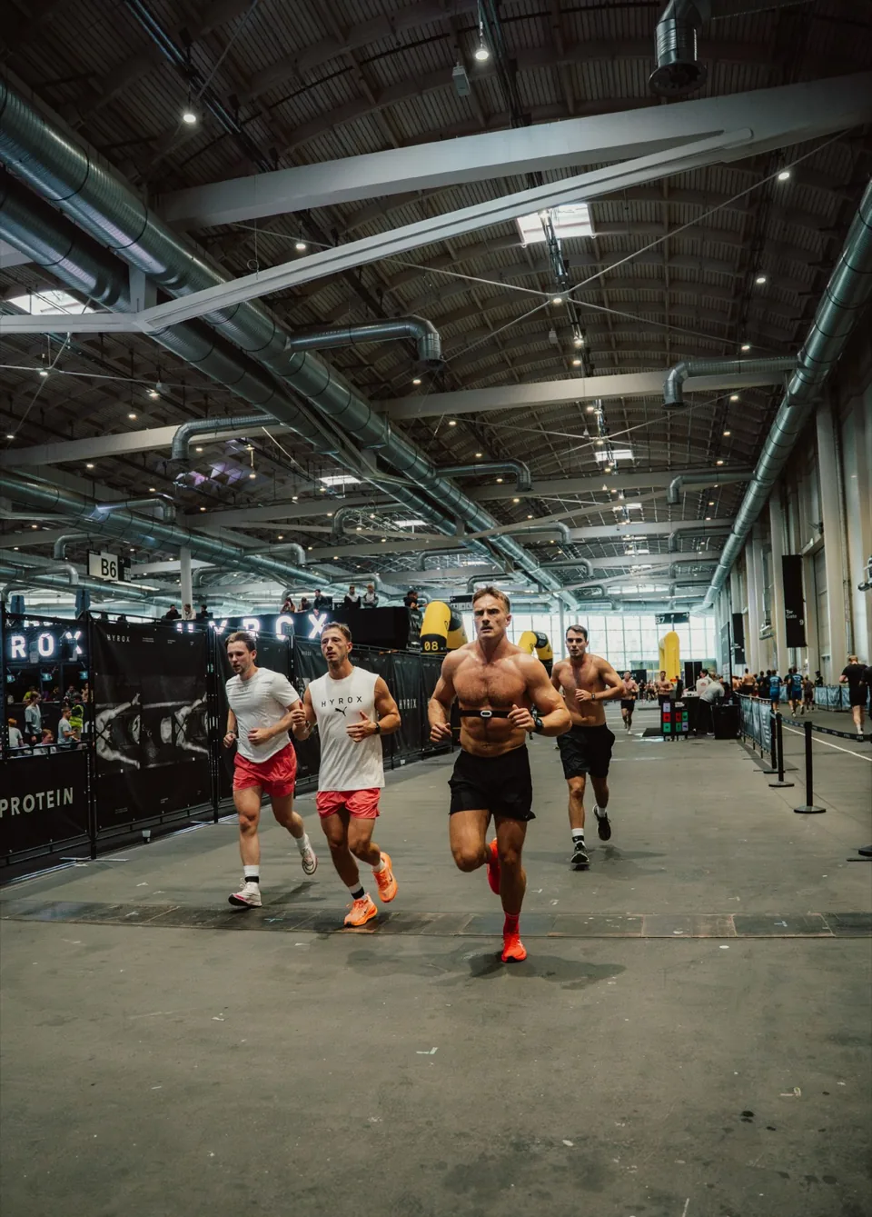 Athletes running through an indoor HYROX race arena.