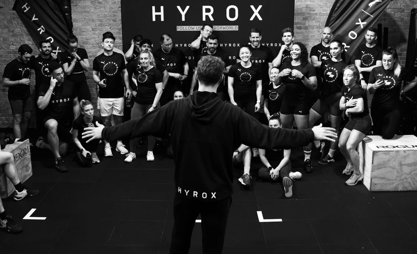 HYROX participants gathered around a coach in a training space