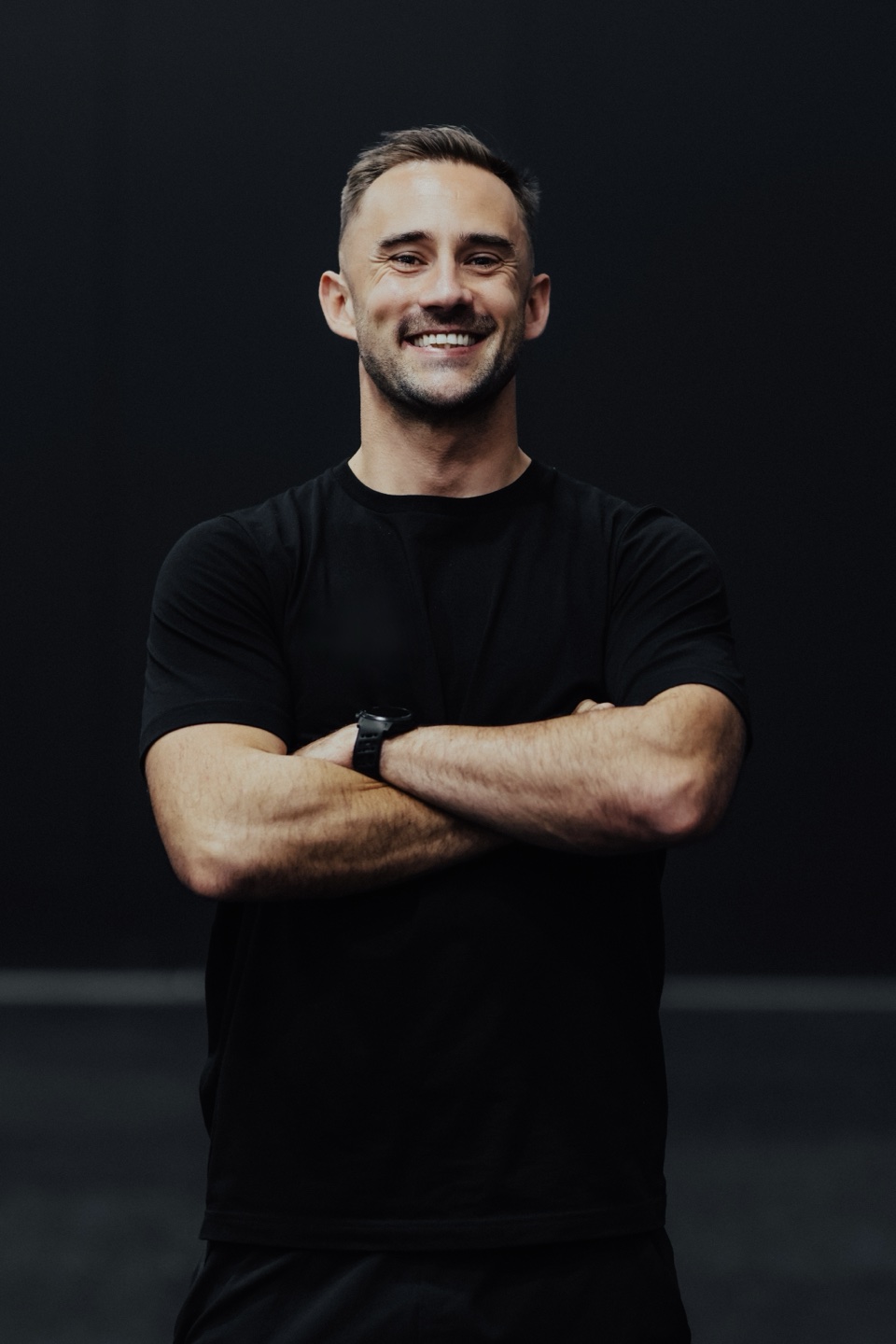 Jay Clark smiling with arms crossed against a dark background